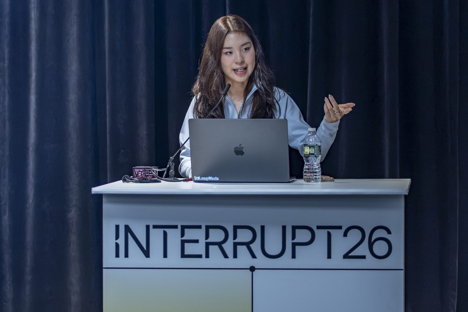 Jess speaking at the Interrupt26 podium with a LangChain sticker on her laptop